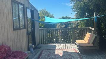 A wooden deck with a blue shade sail, a red patterned sofa, and a beige sofa with cushions.