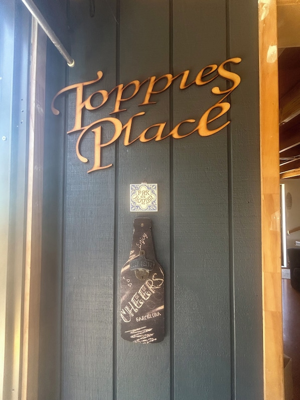 A wooden door with the words "Toppies Place" and a bottle-shaped plaque with "CHEERS" and "BARCELONA" inscribed.