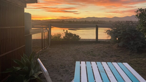 A patio with a view of a sunset over a body of water, a wooden fence, and a table.
