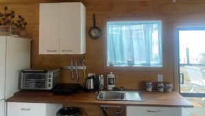 A compact kitchen with wooden cabinets, a toaster, a kettle, and a window with curtains.