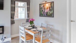 Een eetruimte met een tafel gedekt voor vier personen, een raam met gordijnen, een schilderij aan de muur en een televisie.