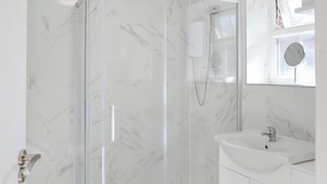 Een badkamer met een douche met glazen wanden, een witte wastafel en een spiegel boven de wastafel.