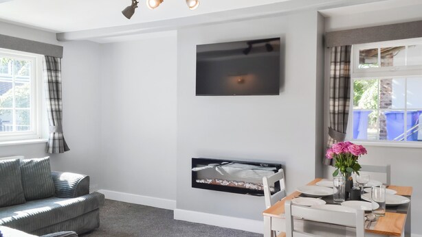 Een moderne woonkamer met een bank, een eettafel voor twee personen, een flatscreen televisie aan de muur en een open haard.