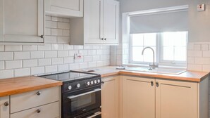 Een keuken met witte kastjes, een zwarte kookplaat en een raam met een witte zonwering.