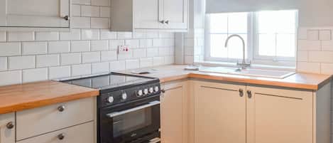 Una cocina con armarios blancos, una estufa negra y una ventana con persiana blanca.