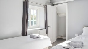 Een slaapkamer met twee bedden, een raam, een radiator en een open deur naar een inloopkast.
