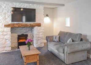 A living room with a stone fireplace, a grey sofa, and a wooden coffee table. - A beautifully restored two-storey, two bedroom cottage sleeping four people. (Filey)