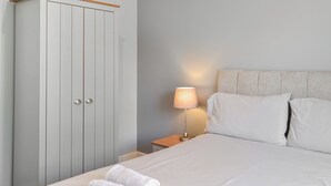 A bedroom with a bed, pillows, a nightstand, a lamp, and a wardrobe. - A beautifully restored single-storey two bedroom cottage sleeping four people. (Filey)
