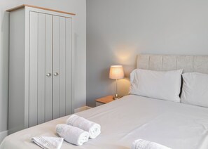 A bedroom with a bed, pillows, a nightstand, a lamp, and a wardrobe. - A beautifully restored single-storey two bedroom cottage sleeping four people. (Filey)