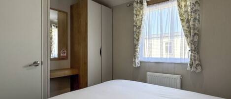 A bedroom with a bed, a wardrobe, a mirror, a window with curtains, and a radiator.