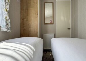 Une chambre d’hôtel avec deux lits, un mur lambrissé, un radiateur, une porte et un miroir.