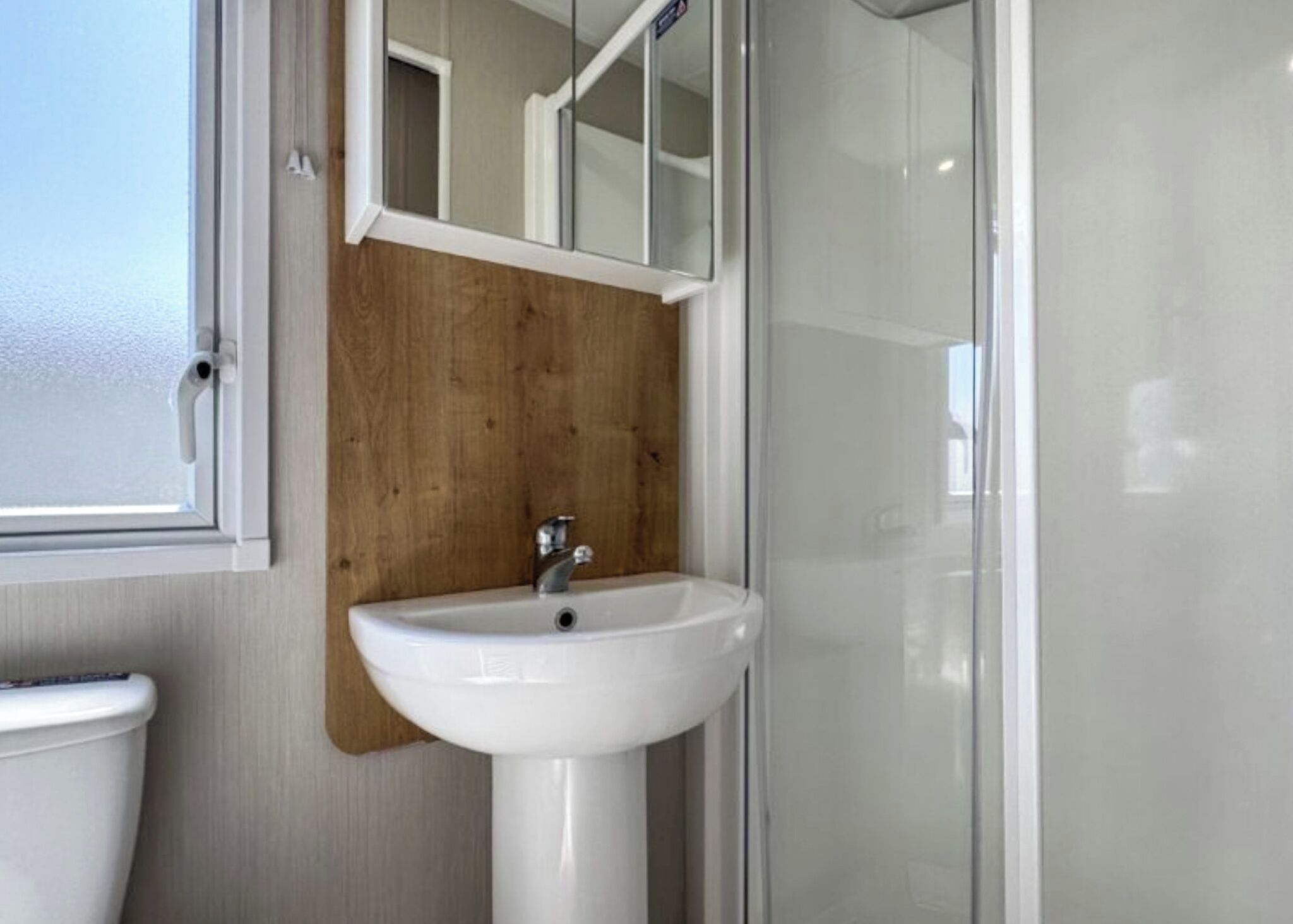 A bathroom with a white sink, wooden panel wall, and a glass shower enclosure.