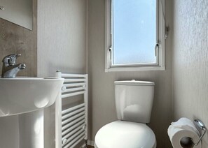 A small bathroom with a white sink, toilet, and a window. - 3 bedroom accommodation in Skegness (Skegness)