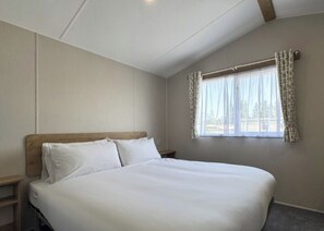 Quarto com cama, janela com cortinas, mesa de cabeceira e cabeceira de madeira.