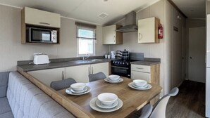 Una cocina compacta con microondas, estufa y lavaplatos, una mesa de comedor con platos y tazones, y un sofá en la sala de estar contigua.