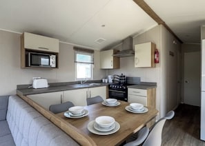A compact kitchen with a microwave, stove, and sink, a dining table with plates and bowls, and a sofa in the adjacent living area.