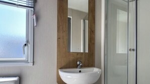 Un baño con lavamanos blanco, pared de paneles de madera, espejo y puerta de ducha de vidrio.