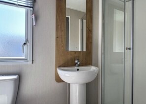 A bathroom with a white sink, a wooden panel wall, a mirror, and a glass shower door.