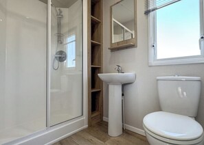A bathroom with a glass-enclosed shower, a pedestal sink, a toilet, and a wooden shelving unit.