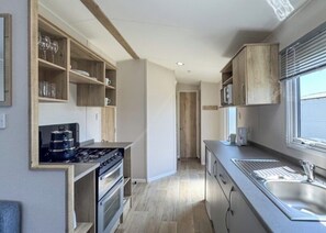 A modern kitchen with built-in appliances, wooden shelves, and a large window.