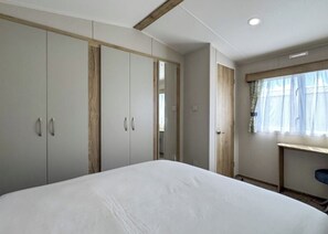 Un dormitorio con una cama grande, armario y escritorio junto a una ventana.