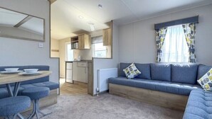 En kompakt opholdsstue med tekøkken, spiseplads og siddeområde med sofa og hynder.