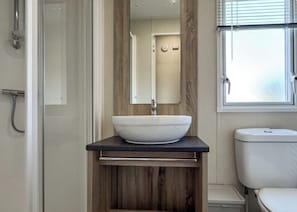 A bathroom with a white sink, wooden vanity, a mirror, a toilet, and a shower. - 1 bedroom accommodation in Skegness (Skegness)