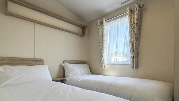 Ein Zimmer mit zwei Betten, einem fensterbelaubten Fenster und einem hölzernen Kopfteil.