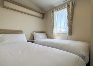 A room with two beds, a window with curtains, and a wooden headboard.