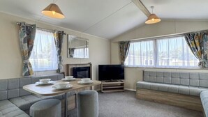 Ein gemütlicher Wohnraum mit Sofa, Esstisch mit Tellern, Fernseher und Vorhängen.