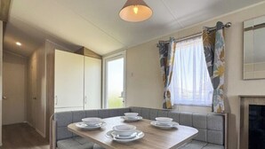 Ein kleiner Essbereich mit einem Holztisch, gedecktem für vier Personen, grau gepolsterten Sitzmöglichkeiten, einem Fenster mit floralen Vorhängen und einem Kamin.