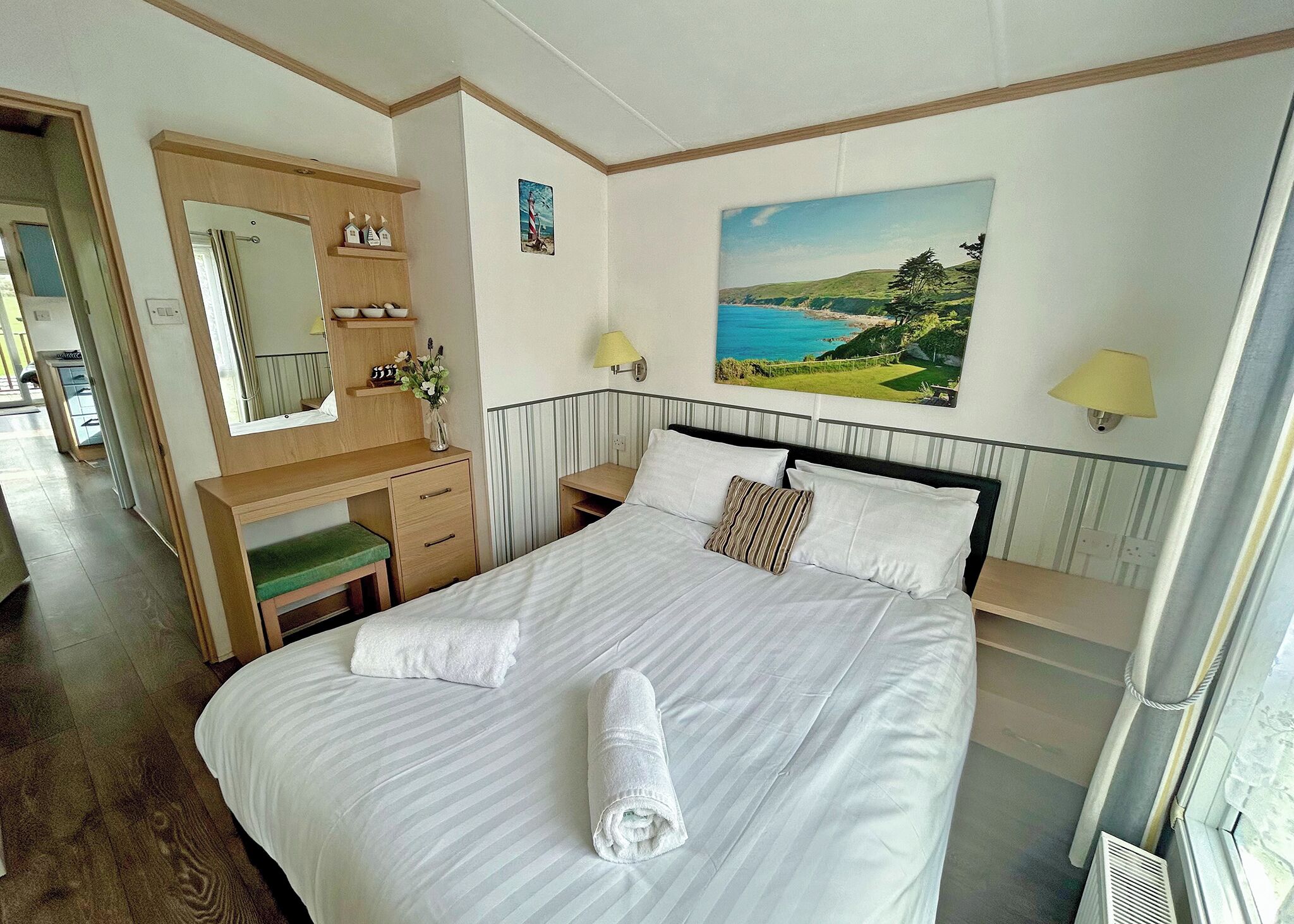 A hotel room with a bed, a desk, a mirror, a painting, and a window.