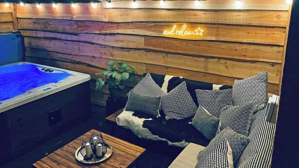 Interior acogedor de una cabaña con pared de madera, un jacuzzi, un sofá con cojines estampados y una mesita con velas.