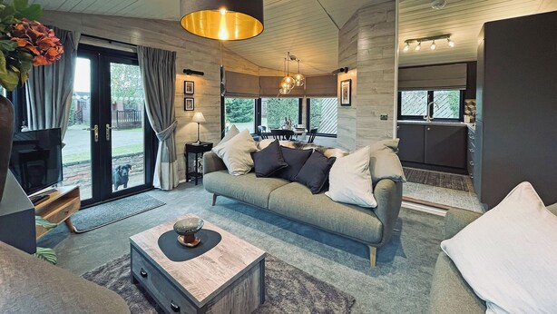 Een moderne woonkamer met een bank, salontafel en een eethoek, met een keuken op de achtergrond.