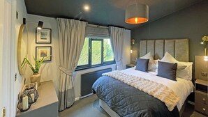 Een moderne slaapkamer met een groot bed, een raam met gordijnen, een radiator en een hanglamp.