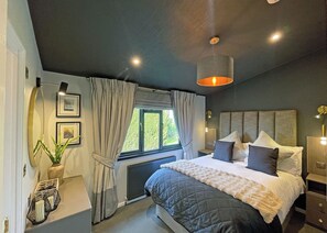 Ein modernes Schlafzimmer mit einem großen Bett, einem Fenster mit Vorhängen, einem Heizkörper und einer hängenden Leuchte.