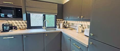 A modern kitchen with grey cabinets, a built-in microwave, and a window with a view of greenery.