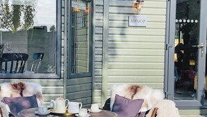 Een gezellig buitenzitje met rieten stoelen en een tafel gedekt voor thee, een bordje met de tekst 'Spruce' en een glazen toegangsdeur.