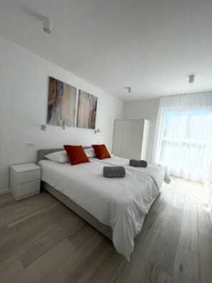 Ein modernes Schlafzimmer mit einem großen Bett, zwei Nachttischen, einem Kleiderschrank und abstrakter Kunst an der Wand.