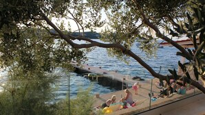 Eine Uferpromenade mit Menschen, die am Wasser entspannen, einem Steg und einer Brücke im Hintergrund.