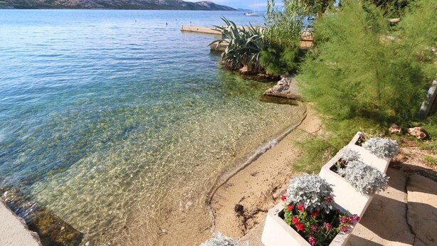 Ein klarer See mit Sandstrand, einer Anlegestelle und Kübelpflanzen.