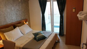 Ein Hotelzimmer mit Bett, Holz-Kopfschild, Nachttisch, Vorhängen und einer Tür mit Handtuchhalter.