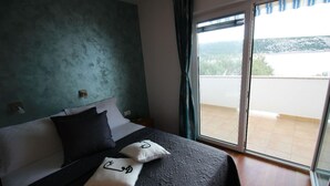 Ein Schlafzimmer mit Bett, Kissen, einem Fenster und Blick auf einen Balkon.
