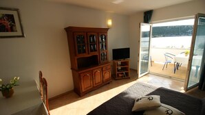 Une chambre à coucher comprenant un lit, une armoire en bois, un téléviseur, une table à manger avec des chaises, et un balcon avec une table et des chaises.