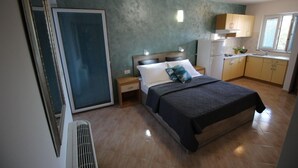 Un dormitorio con cama, mesitas de noche, una ventana y un kitchenette.