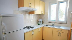 Una cocina con refrigerador, estufa, pileta y ventana con persianas.