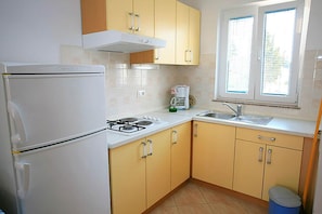 Eine Küche mit Kühlschrank, Herd, Spüle und Fenster mit Jalousien.