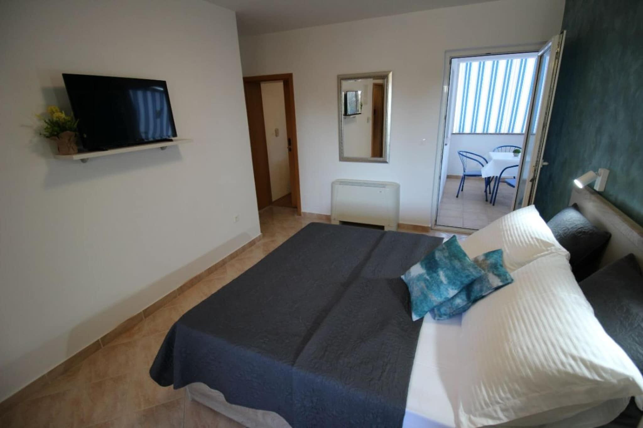 A bedroom with a bed, a TV on a shelf, a mirror, and a view of a balcony with chairs.