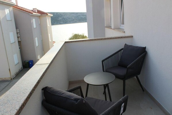 Ein Balkon mit einem kleinen Tisch und zwei Stühlen, mit Blick auf ein Gewässer und Gebäude.