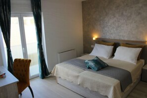 Ein Hotelzimmer mit einem Bett, einem Sessel, einem Schreibtisch und einem Fenster mit Vorhängen.
